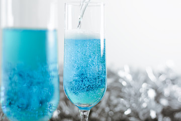 Two glasses with cold light blue champagne on white background with silver decoration. Side view horizontal. Close-up, copy space