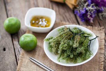 sea grapes or green caviar with spicy sauce on wooden background