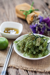 sea grapes or green caviar with spicy sauce on wooden background