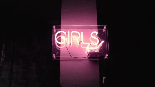 Hand held shot of huge neon sign glowing in dark of word girls, representing direction to bathroom or symbol of feminism underground culture in cafe, bar or art gallery
