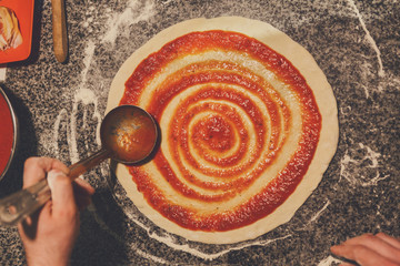Chef hand spreading tomato paste on pizza base