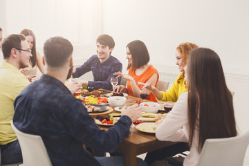 Group of happy young people talking at dinner table, friends party
