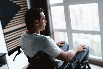 The disabled person in a wheelchair sits in front of a large panoramic window and looks into it. He...