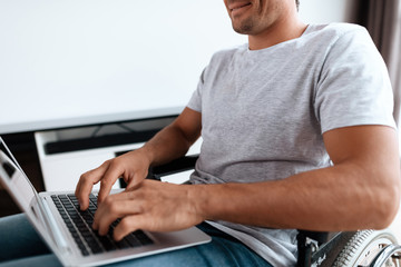 The disabled person sits in a wheelchair in front of a large panoramic window. He has a laptop on...
