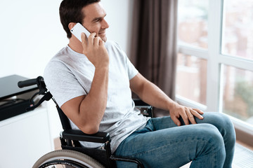 The disabled person sits in a wheelchair in front of a large panoramic window. He is talking to...