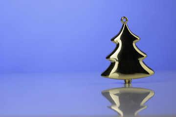 Albero di Natale in miniatura color oro che si riflette nella superficie con sfondo azzurro