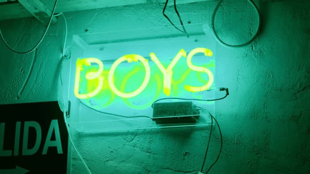 Hand held shot of huge neon sign glowing in dark of word boys, representing direction to bathroom or symbol of underground culture in cafe, bar or art gallery, vintage retro effect