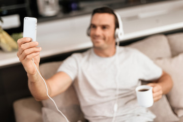 The disabled person is sitting on the couch. He listens to music and makes selfies on his...