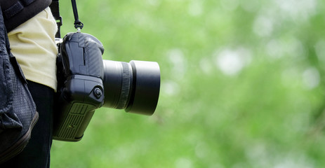 Close up of young man holding DSLR camera in the garden.