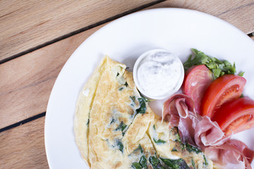 Scrambled eggs with ham on a plate on the wooden table. Tomato and sour cream on the side.