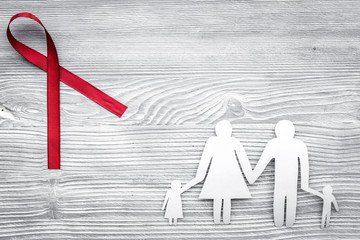 Red ribbon for HIV, AIDS, substance-abuse and anorexia awareness near paper silhouette of family on grey wooden background top view copyspace