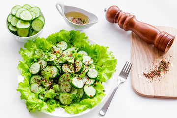 Salad with fresh cucumbers and lettuce near paperbox and gravy boat. White background