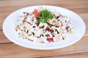 Healthy grilled red meat salad with cheese and croutons. Bacon and lettuce slices in a white plate on a wooden table.