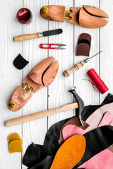 Shoemakers' craft. Tools, wooden last, pieces of leather on white wooden background top view