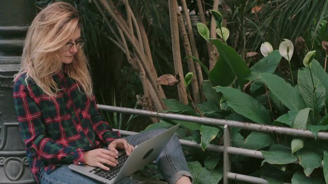 Young creative freelance professional or startup office worker, blonde cute woman works on laptop at park, developer writes coe or student chats with friends. space for text