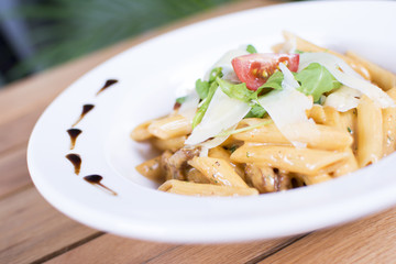 Plate of delicious pasta with savory minced beef and tomato sauce garnished with parmesan cheese and basil.