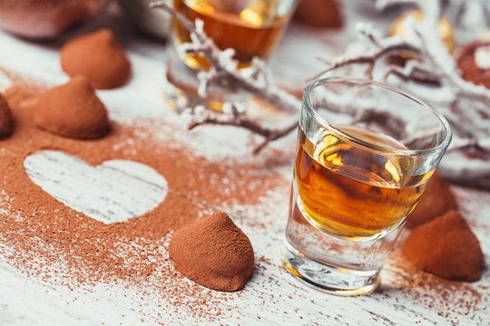 Whiskey or liqueur, truffle chocolate candies in cocoa powder and christmas decorations on white wooden background.