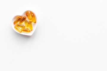 Treat heart. Pills in bowl in shape of heart on white background top view copyspace