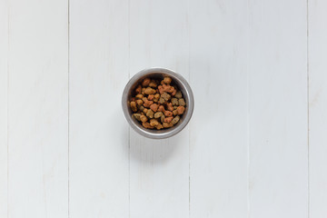 Obraz na płótnie Canvas Dry pet food in bowl on white wooden background top view in the center