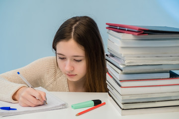 Exhausted and absorbed teenager doing her homework among stack of books