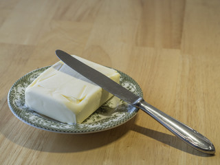 close up whole butter cube on green plate with knife on wooden table