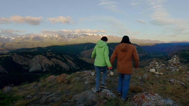 A pair of lovers walking through picturesque hills holding hands 4k. Mountain landscape on the background