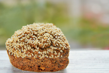 Freshly baked raisins cake with sesame seeds isolated on gray wooden table. Muffin on blurred nature background. Close up view