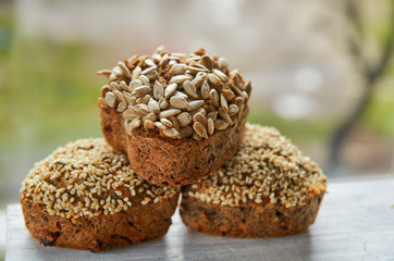 Three freshly baked raisins cakes with sesame and sunflower seeds isolated on gray wooden table. Three muffins on blurred nature background. Close up view