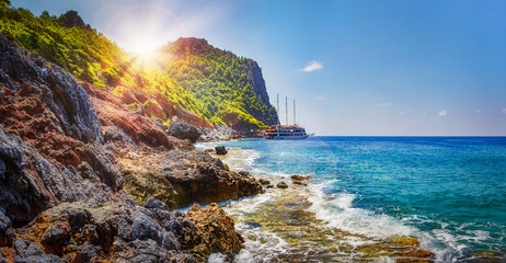 Tropical rocky beach on sunny summer day in Alanya, Turkey. Sea and mountains landscape with waves. Lagoon bay. Panoramic view on paradise coastline. Summer vacation nature. Adventure and travel. - obrazy, fototapety, plakaty
