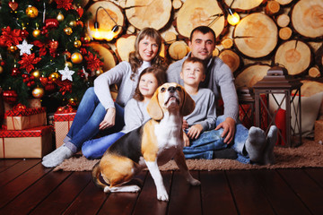 Happy family celebrating Christmas and New year at the beautiful Christmas tree in your home with her Beagle dog. - Powered by Adobe