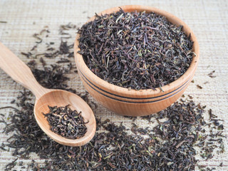 Loose tea in a wooden dish with a spoon.

