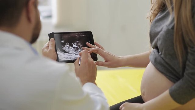 the doctor shows a picture of an ultrasound on a tablet to a pregnant woman. A happy future mother admires a picture of her baby's ultrasound.