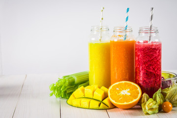 Multicolored smoothies in bottles of mango, orange, banana, celery, berries, on a wooden table.