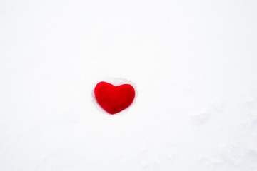 Red plush heart abandoned on white snow.