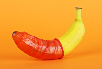 Red condom and banana on colored background