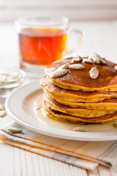 Pumpkin pancakes with honey and pumpkin seeds in plate on white wooden background.