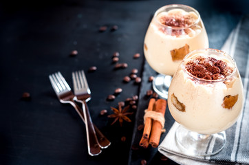 tiramisu in a glass decorated with coffee beans on a dark background, concept of a sweet and luxurious life