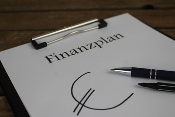 Finanzplan auf einem Klemmbrett mit Stiften vor Holzhintergrund 1