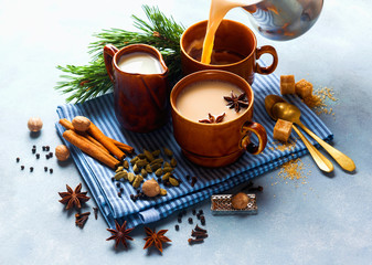 Obraz na płótnie Canvas Pouring Masala tea chai latte traditional hot Indian teatime ceremony sweet milk with spices, herbs organic infusion healthy beverage in porcelain cup n blue table background.