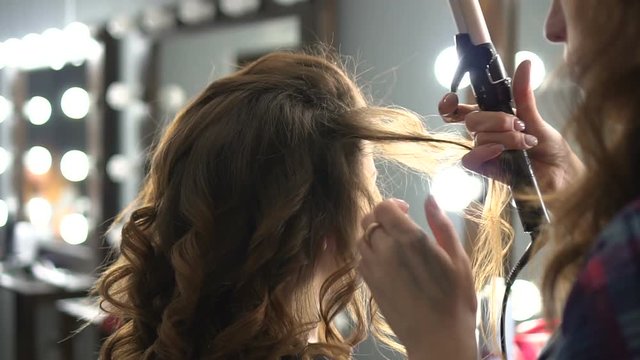 Hairdresser doing wrap curling brown hair in a beauty salon with iron