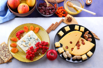 Cheese with mold, fruit, hard cheese with holes on a dark blue background, cheese on a black plate, fruits, nuts, honey, jam, Christmas dinner, multicolored background, retro style