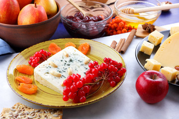 Cheese with mold, fruit, hard cheese with holes on a dark blue background, cheese on a black plate, fruits, nuts, honey, jam, Christmas dinner, multicolored background, retro style