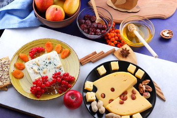 Cheese with mold, fruit, hard cheese with holes on a dark blue background, cheese on a black plate, fruits, nuts, honey, jam, Christmas dinner, multicolored background, retro style
