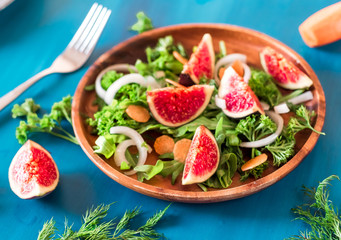 Autumn salad of arugula, figs in a brown earthenware plate on a blue background. top view