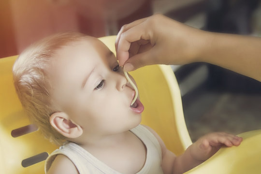 Mom feeds the little baby boy noodles in highchair