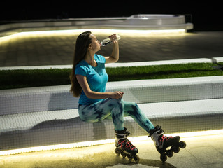 Sports roller girl sitting after skating at night city with lights in bokeh. Outdoor night city...