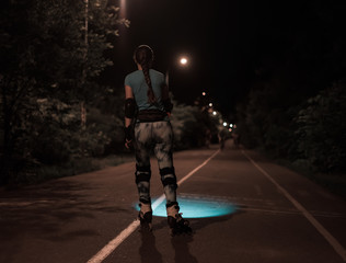 Fototapeta na wymiar Sports roller girl skating at night using flashlight or torchlight. She is searching for way on the road.