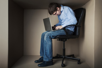 teenager, student in small office working on laptop, in an uncomfortable position