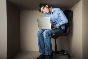 teenager, student in small office working on laptop, in an uncomfortable position