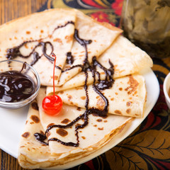 Pancakes with chocolate and cherry on a white plate.